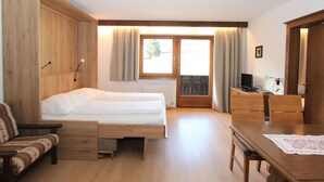 Une chambre à coucher comprenant un lit, un bureau, une chaise, une armoire et une fenêtre avec des rideaux.