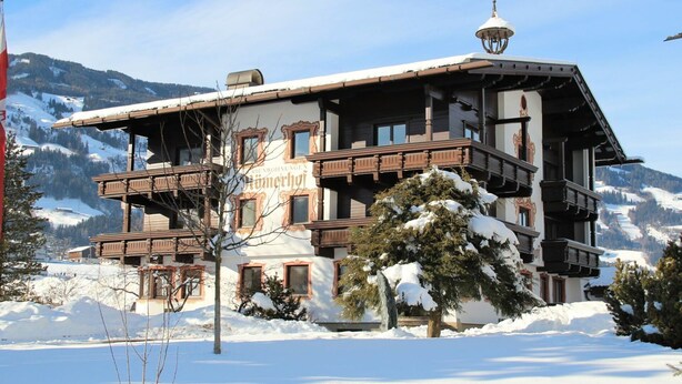 Un bâtiment de style chalet traditionnel, doté d’un balcon, entouré d’arbres couverts de neige et avec des montagnes en arrière-plan.