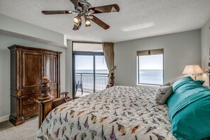 Une chambre avec un grand lit, un ventilateur de plafond, une vue sur l’océan et une commode en bois.
