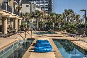 A pool area with lounge chairs, a blue inflatable raft, and palm trees.