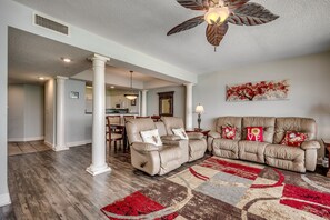 A spacious living room with a beige leather sofa set, a patterned rug, and a ceiling fan.