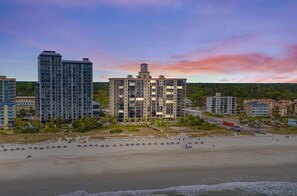 Un hôtel situé en bord de mer, composé de plusieurs immeubles de grande hauteur, avec une plage de sable fin et un ciel dégagé.