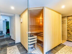 A sauna with a wooden interior, a glass door, and a stone wall in the background. - Charming Villa in Harze (Aywaille)