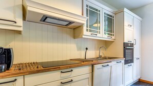 Una cocina moderna con armarios blancos, encimera de madera, horno empotrado y pileta de acero inoxidable.