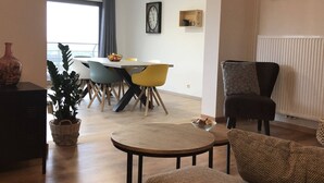 Uma sala de estar moderna com área de jantar, apresentando uma mesa de centro redonda, um sofá e uma mesa de jantar com cadeiras coloridas.