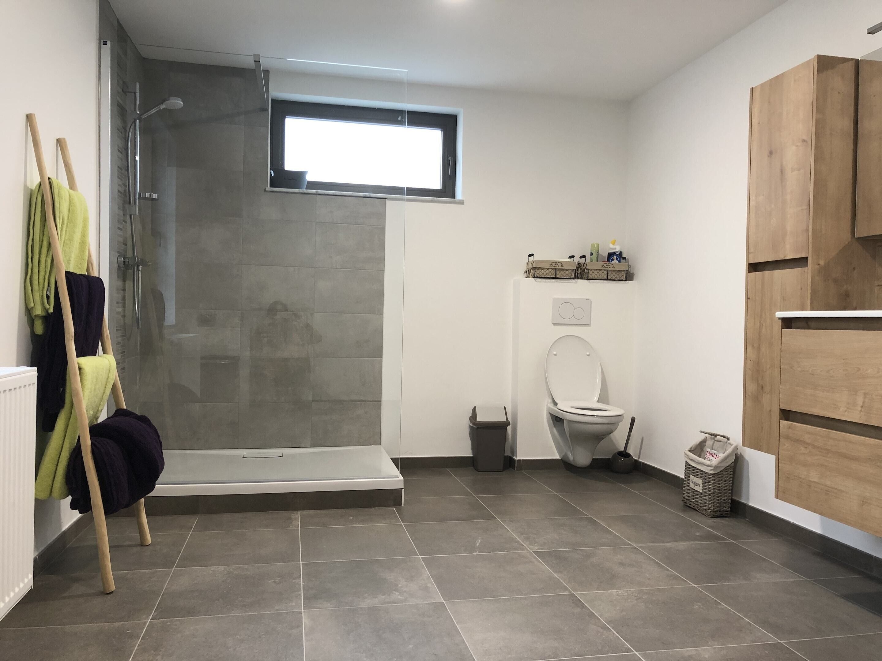 A modern bathroom with a shower, toilet, and a small window.