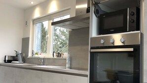 Cozinha moderna com eletrodomésticos de aço inoxidável, janela com vista para árvores e forno embutido.