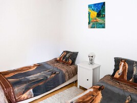 A bedroom with two beds, each with a horse-themed bedspread, a white nightstand with a lamp, and a painting of a night scene by van Gogh on the wall.