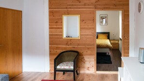 Habitación con paredes de paneles de madera, un espejo, una cama con colcha estampada, una silla con cojín floral y suelo de madera.