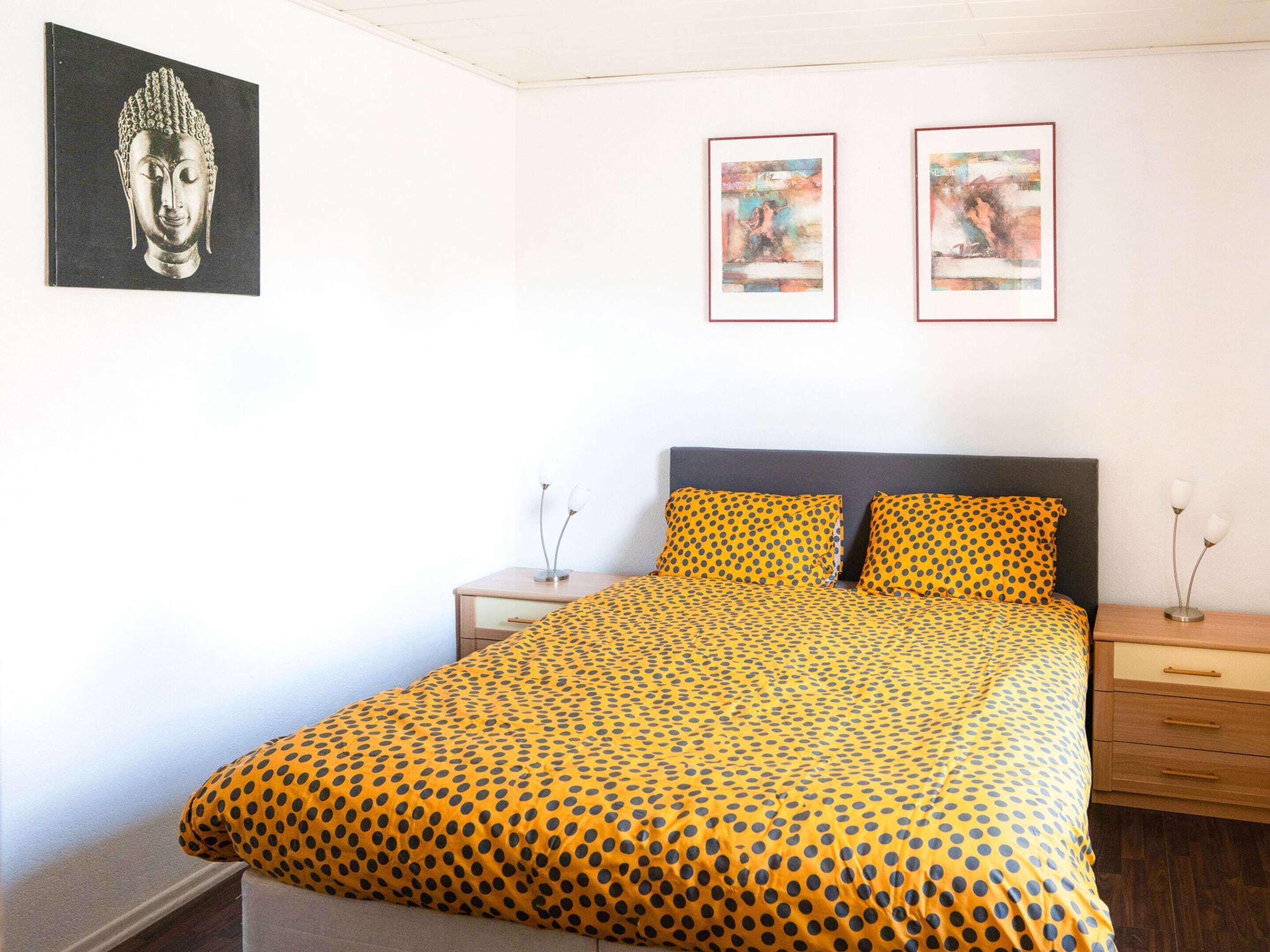 A bedroom with a bed, two bedside tables, and two framed pictures on the wall.