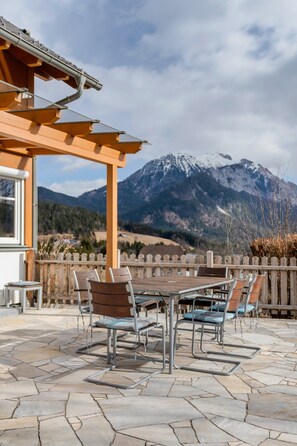 An outdoor patio with a wooden table and chairs, a pergola, and a view of snow-capped mountains.
