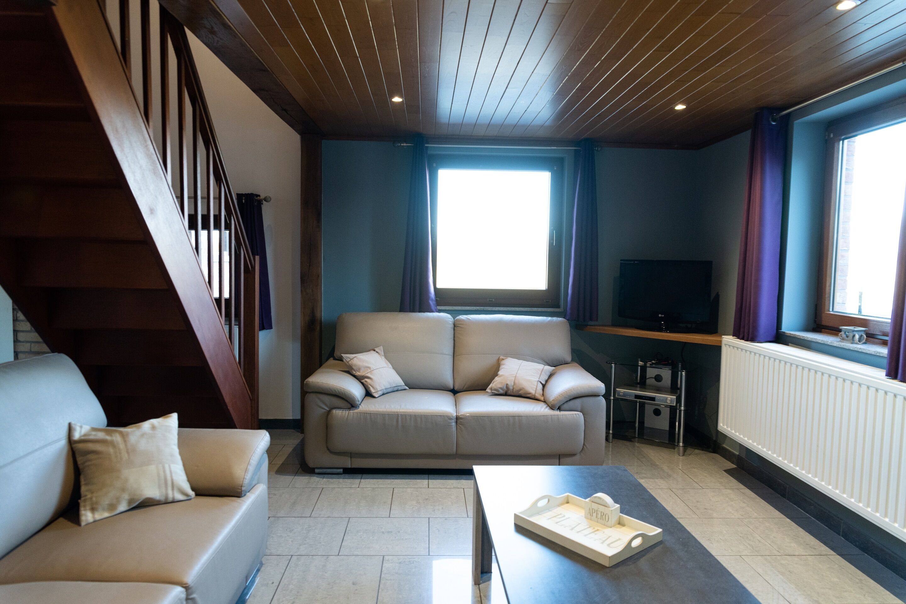Una sala de estar con sofá, una mesa de centro, televisor y una ventana con cortinas.