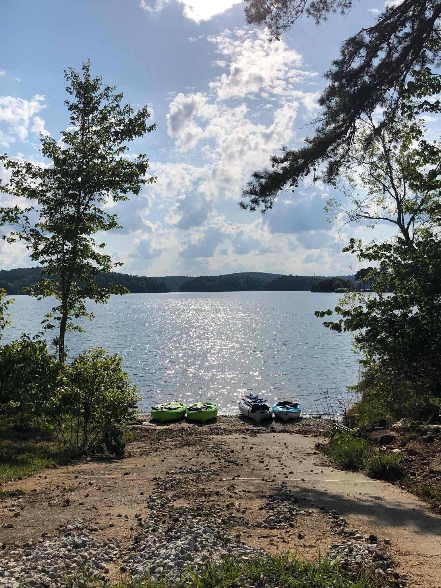 Une vue sur le lac, avec des kayaks sur une plage de sable, entourée d’arbres et sous un ciel dégagé.