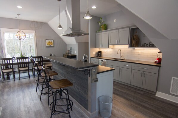 A modern kitchen with a central island, bar stools, and a dining area with a bench. - Clean, Modern, Lake Keowee Retreat Near Clemson (Six Mile)