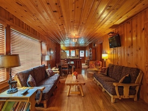 Cozy cabin-style interior with a central dining area, two sofas, a coffee table, and a television.