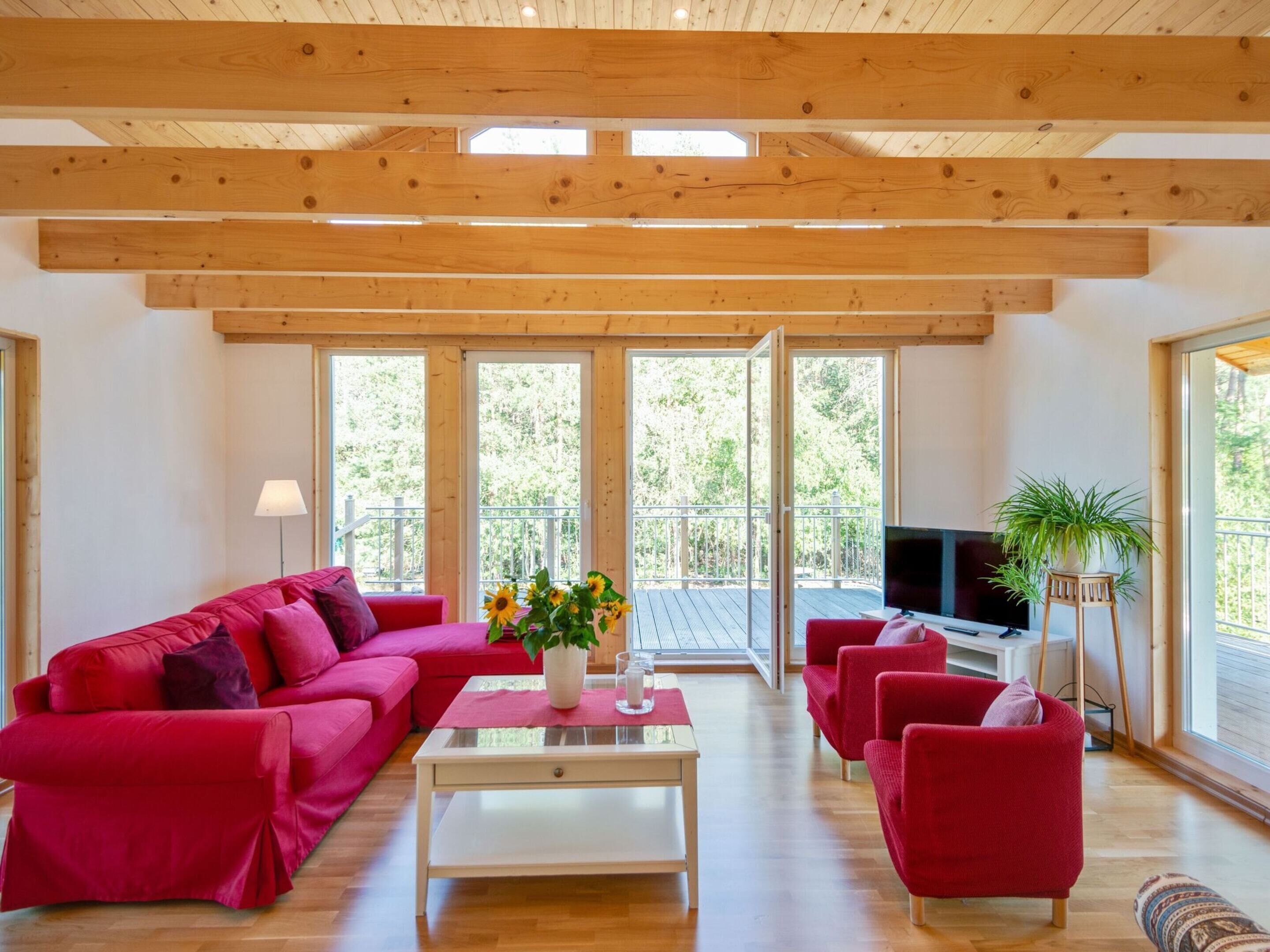 Un soggiorno spazioso con soffitto in legno, ampie finestre, un divano rosso, un tavolino da caffè e una TV.
