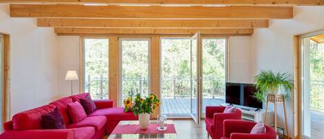 Un soggiorno spazioso con soffitto in legno, ampie finestre, un divano rosso, un tavolino da caffè e una TV.