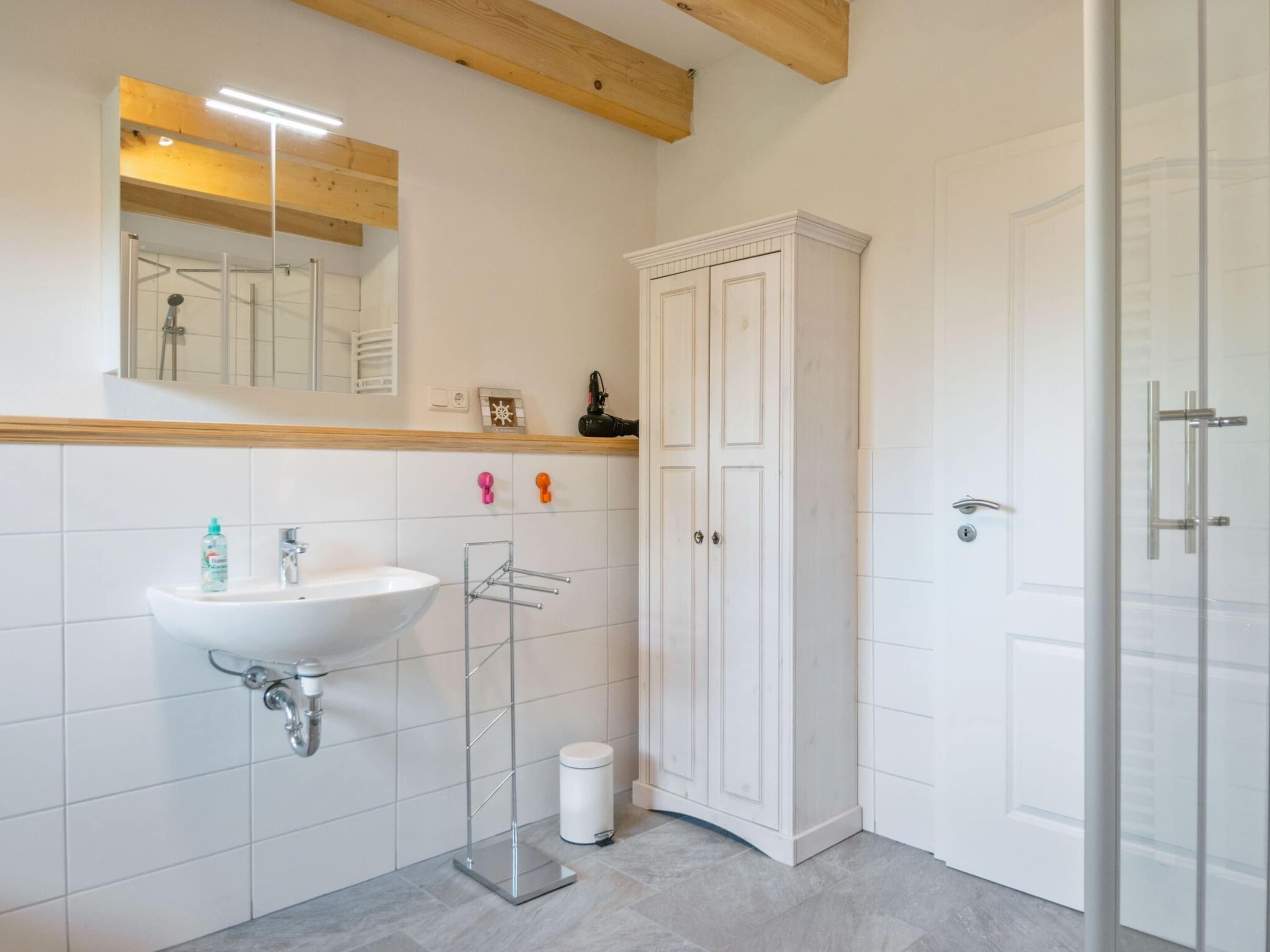 A modern bathroom with a white sink, mirror, and cabinet, and a shower area.