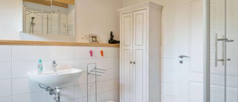 A modern bathroom with a white sink, mirror, and cabinet, and a shower area.