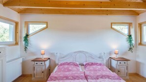 Ein Schlafzimmer mit Holzboden, zwei Fenstern, einem Bett mit blumigem Rosa-Bettzeug, Nachttischen mit Lampen und einem Heizkörper.
