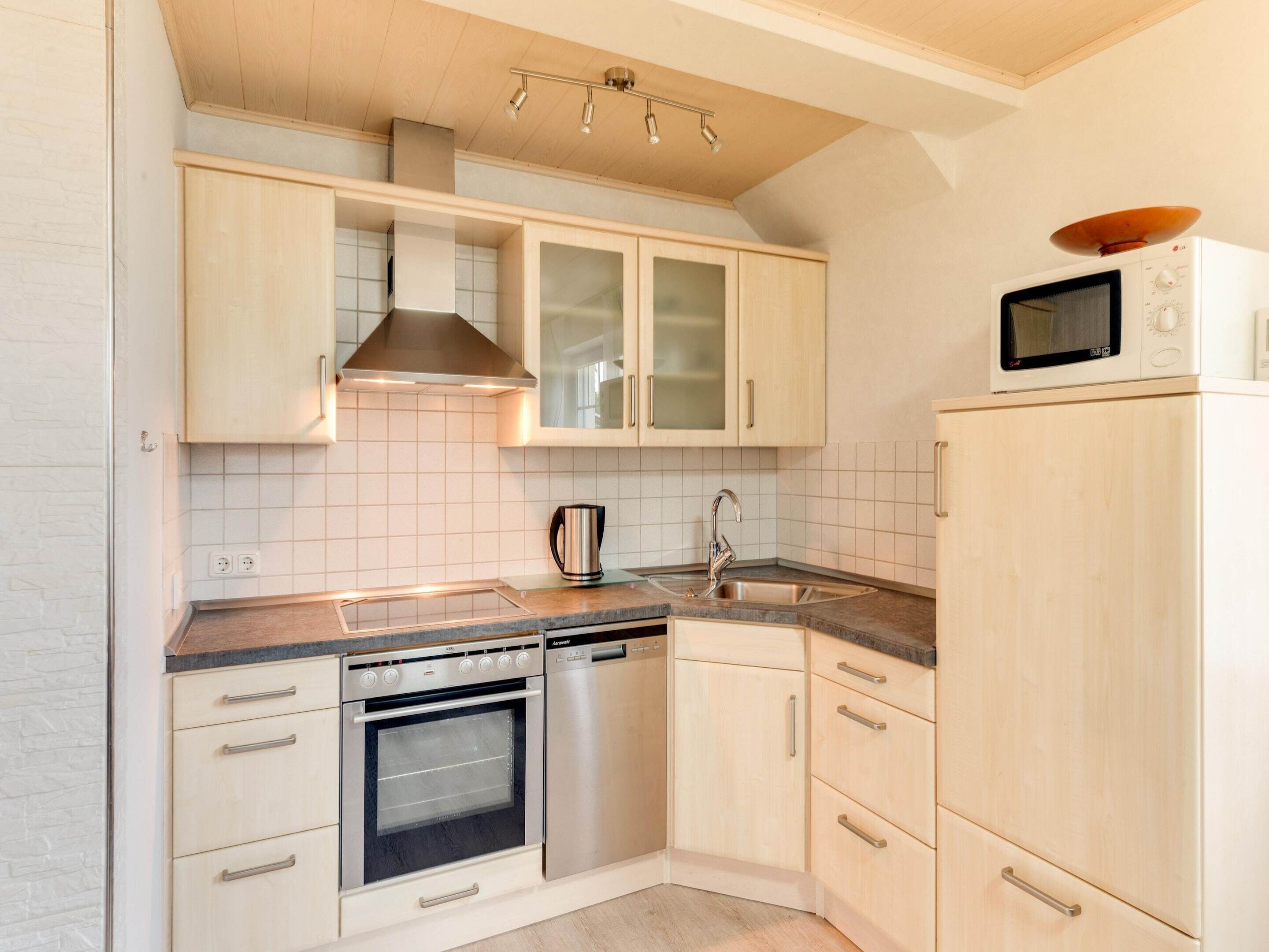 Een moderne keuken met lichte houten kastjes, een roestvrijstalen oven, een vaatwasser en een magnetron.