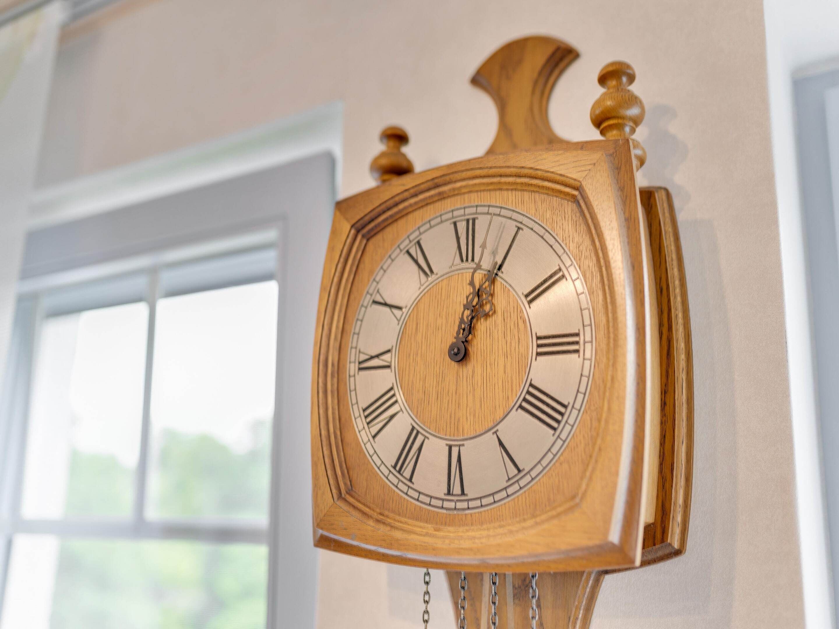 A wooden wall clock with Roman numerals and a pendulum.