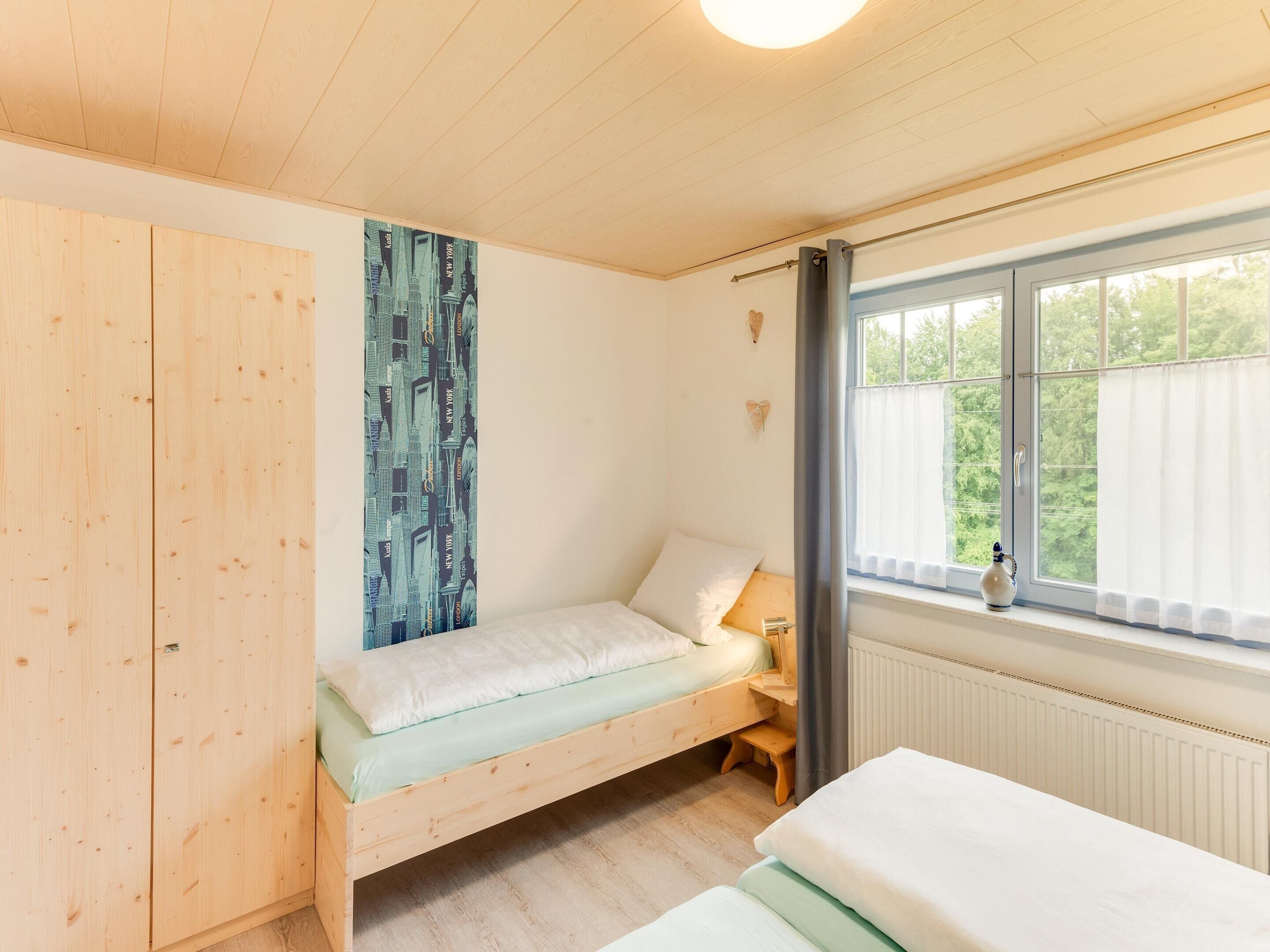 A small, cozy room with a wooden bed, a window with curtains, and a radiator.