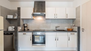 Una cocina moderna con armarios blancos, horno empotrado, estufa y cafetera.