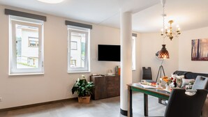 Una sala de estar moderna con comedor, ventanas amplias, televisor de pantalla plana y una lámpara de araña.