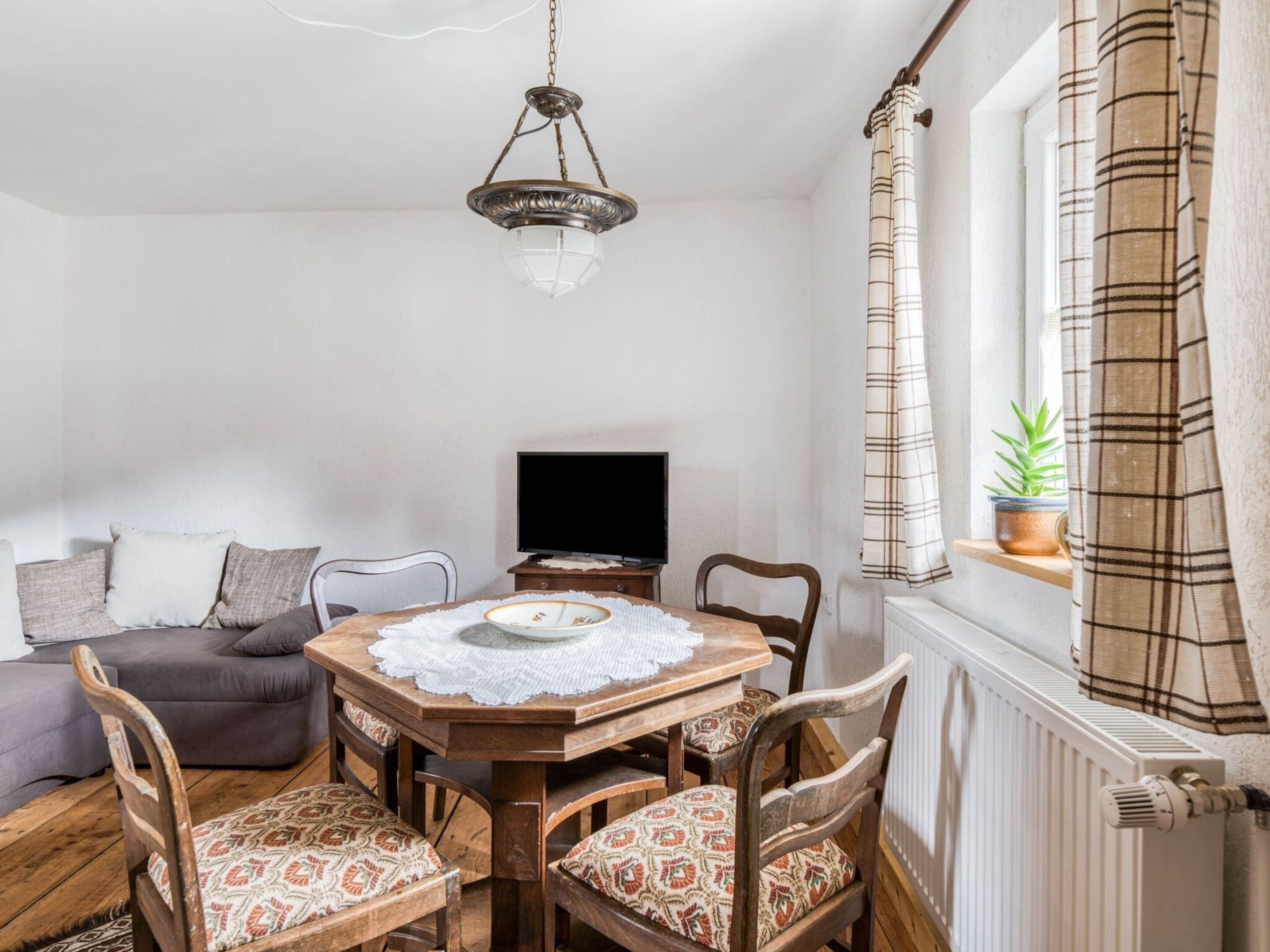 A cozy dining area with a wooden table and chairs, a television on a stand, and a window with curtains.