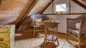 A cozy attic room with wooden walls and a sloped ceiling. There are two wicker chairs with cushions, a small round table, and a window with a view. - Escape Near River, Wolfsberg (Sangerhausen)