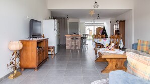 A living room with a television, wooden furniture, and a dining area with chairs and a table. - Renovated Village House With Enclosed Garden (Saint-Louis)