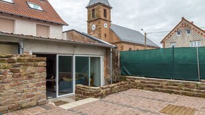 A building with a brick facade, a tower with a clock, and a covered patio area. - Renovated Village House With Enclosed Garden (Saint-Louis)
