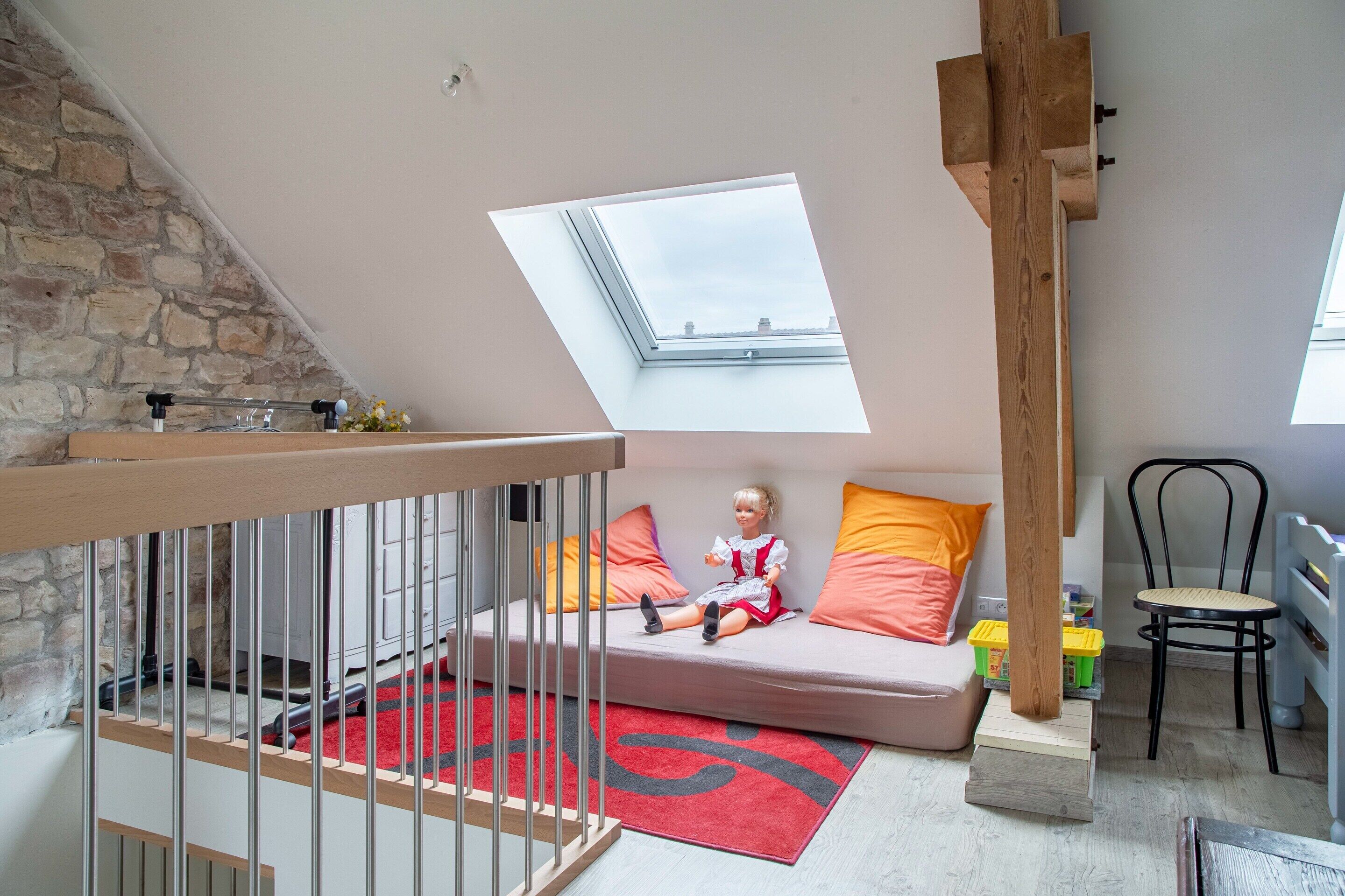 A loft bedroom with a skylight, a wooden staircase, a red rug, and a child's play area.