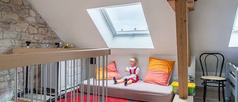 A loft bedroom with a skylight, a wooden staircase, a red rug, and a child's play area.