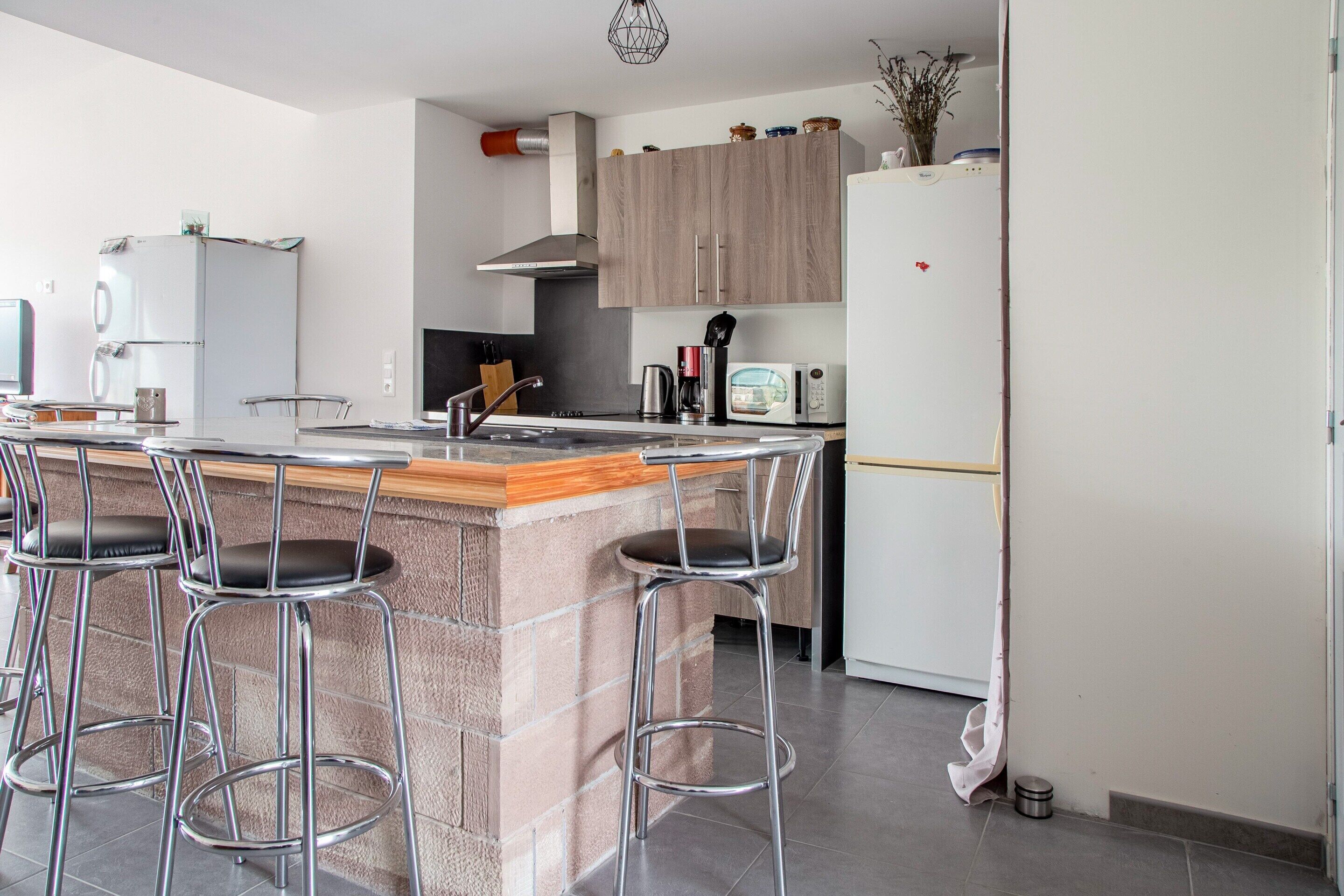 A modern kitchen with a central island, bar stools, a refrigerator, and a microwave.