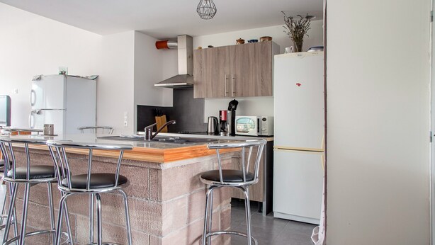 A modern kitchen with a central island, bar stools, a refrigerator, and a microwave. - Renovated Village House With Enclosed Garden (Saint-Louis)