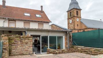 Un edificio tradicional con fachada de piedra, una torre de campanas y una extensión moderna con puertas de vidrio.