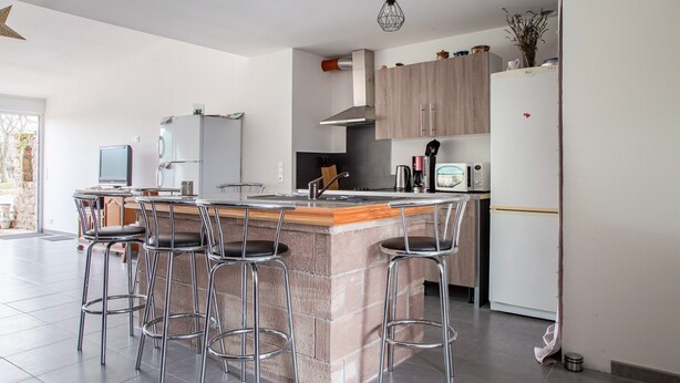 A modern kitchen with a central island, bar stools, a built-in oven, and a refrigerator. - Renovated Village House With Enclosed Garden (Saint-Louis)
