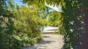 A pathway surrounded by dense greenery, leading to a paved area with a vehicle. - Holiday Home in Barry-d'islemade With Pool (Barry-d'Islemade)