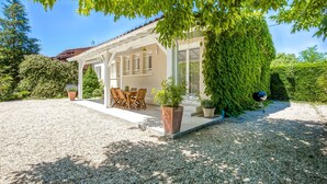 A covered outdoor seating area with a table and chairs, surrounded by gravel and potted plants. - Holiday Home in Barry-d'islemade With Pool (Barry-d'Islemade)