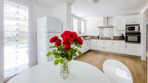 A modern kitchen with white cabinetry, a white dining table, and a vase with red flowers. - Holiday Home in Barry-d'islemade With Pool (Barry-d'Islemade)