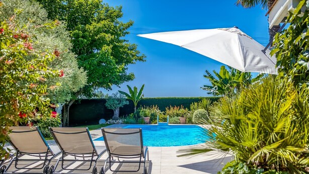A poolside area with lounge chairs and a white umbrella. - Holiday Home in Barry-d'islemade With Pool (Barry-d'Islemade)