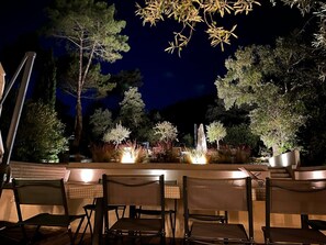 Un espace extérieur aménagé pour les repas, avec des chaises et des tables, entouré d’arbres et agrémenté d’un élément décoratif lumineux.