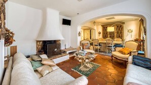 Amplio salón con chimenea, asientos cómodos y un comedor visible a través de un arco.