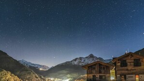 Una cabana de muntanya amb façana de fusta, un balcó i una vista d'un vall amb llums a la distància.