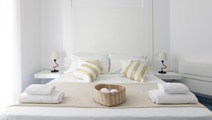 Een opgemaakt bed met witte lakens, twee nachtkastjes met lampen, en een geweven mand op het bed.