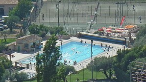 A large rectangular swimming pool surrounded by a fence, with a few people swimming and walking around. - Village House in Fayence With Castle Views (Fayence)