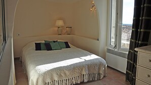 A bedroom with a bed, two bedside lamps, a window with a view, and a dresser. - Village House in Fayence With Castle Views (Fayence)