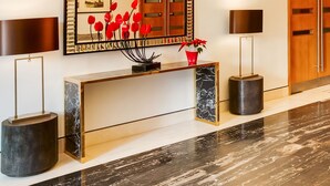Un'accoglienza moderna con una console in marmo, un grande specchio e un'elegante composizione floreale rossa.